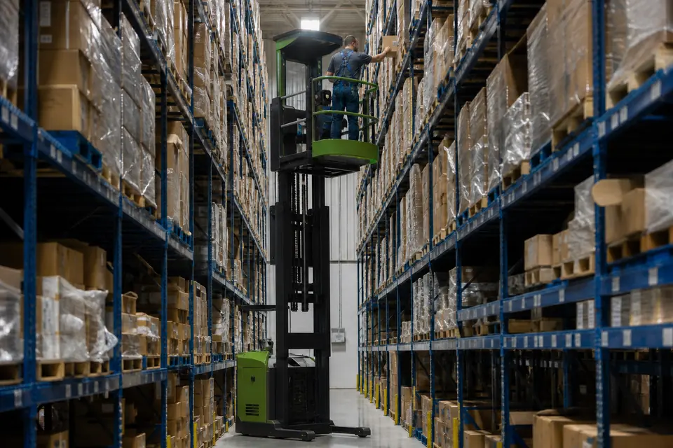 Green high-level order picker in a warehouse aisle