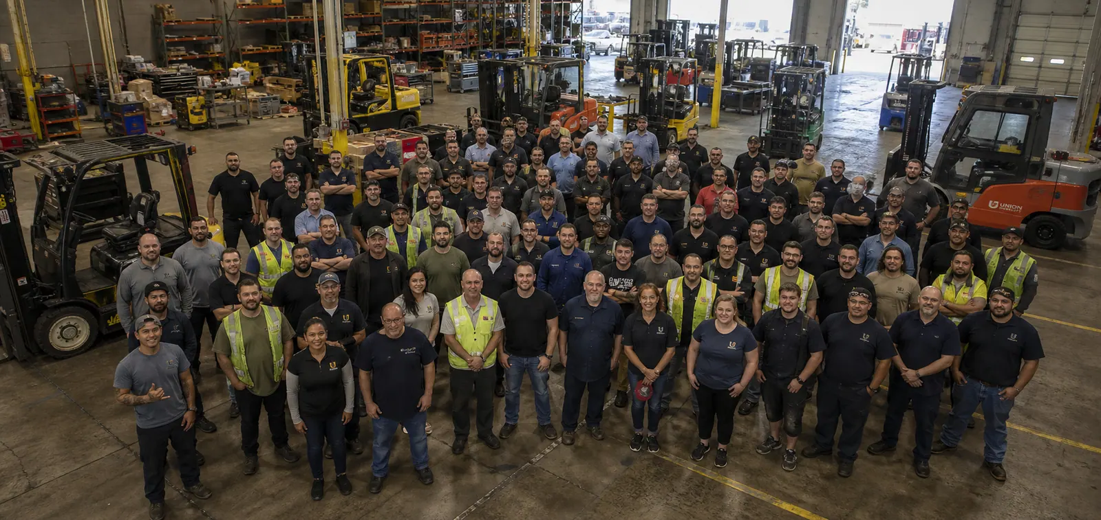 Large, diverse warehouse workforce gathered with forklifts inside a material handling facility