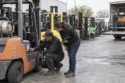 Business buyer and equipment technician inspecting a used forklift in a dealer yard